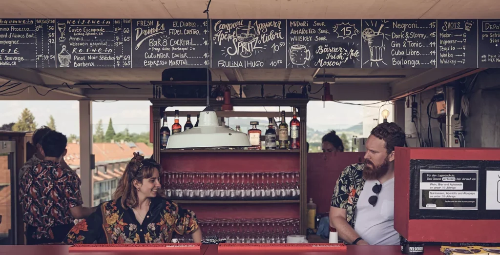 Mitarbeitende im Sommer die in farbigen Hemden hinter der Bar arbeiten,.