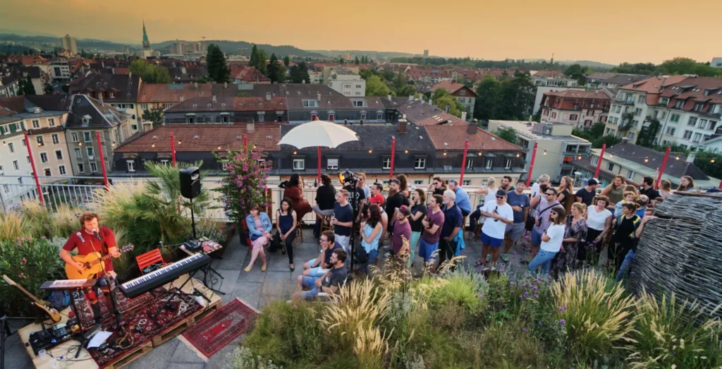 Aufnahme eines Konzerts mit Besuchern auf einer Dachterrasse in gemütliche Abendstimmung.