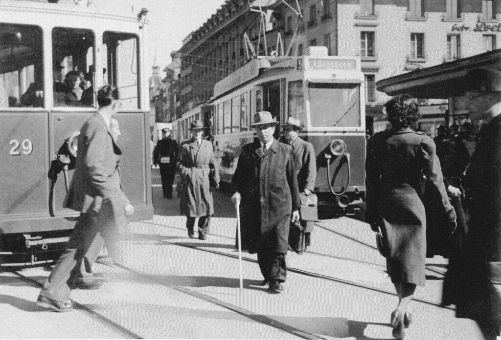 Schwarz/Weiss Aufnahme von einem Mann der draussen mit einem Blindenstock über die Strassen von Bern lauft. 