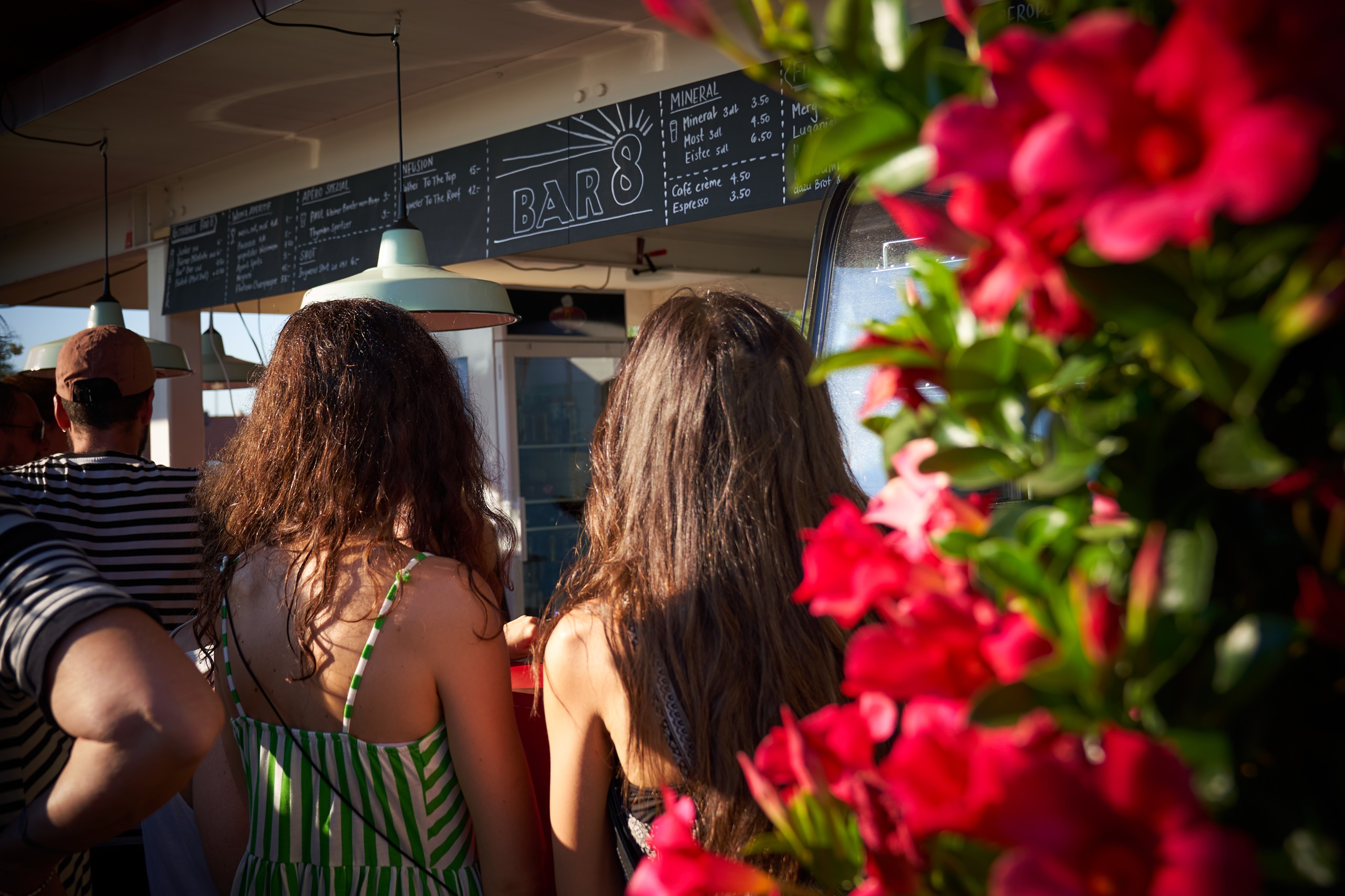 Personen die vor einer Bar stehen und das Menu oberhalb der Bar betrachten.