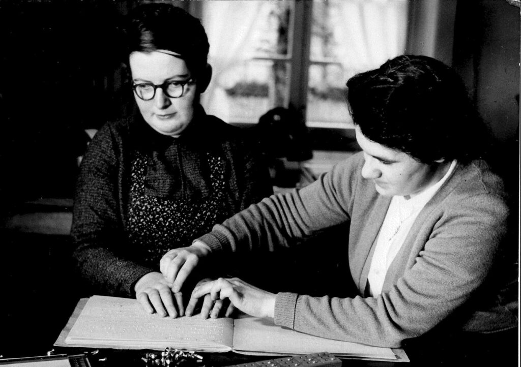 Schwarz/Weiss Aufnahme von zwei Frauen welche gemeinsam die Blindenschrift lernen. 