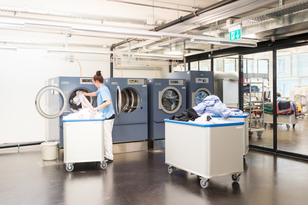 Eine Frau die eine Wäsche in einer Industriewaschmaschine wäscht.
