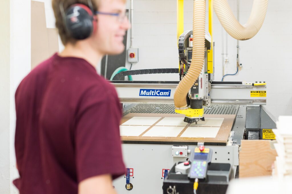 Junger Mann der im Betrieb vom B arbeitet und an einer Schreinermaschine steht.