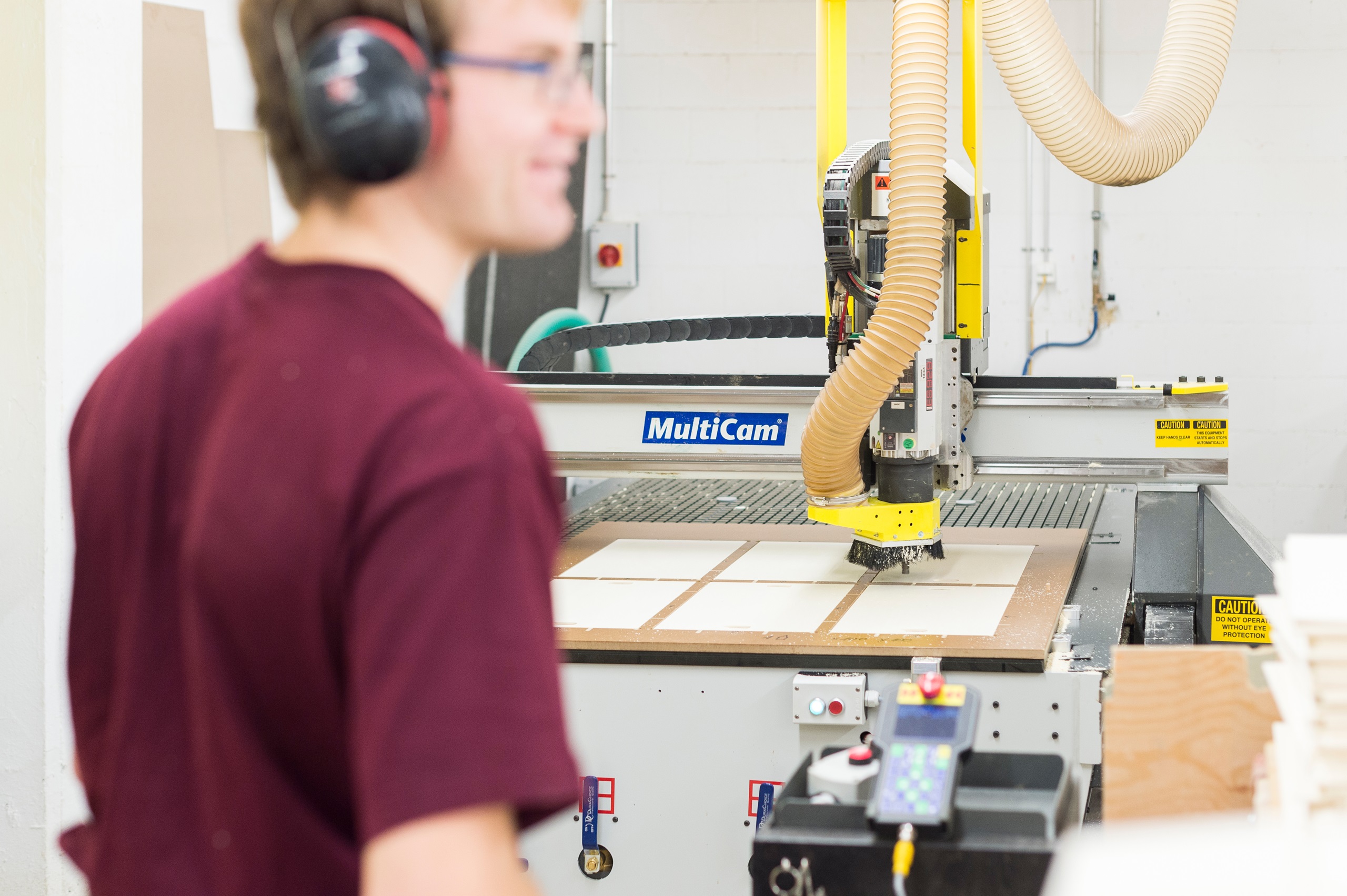 Junger Mann der im Betrieb vom B arbeitet und an einer Schreinermaschine steht.