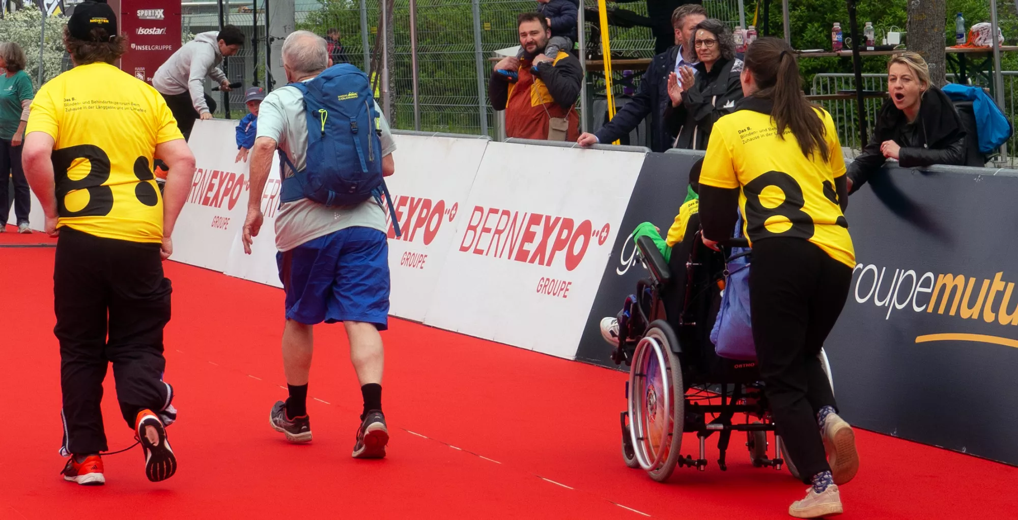 Bild zeigt Menschen, die an einem Laufwettbewerb teilnehmen, darunter auch welche in einem Rollstuhl