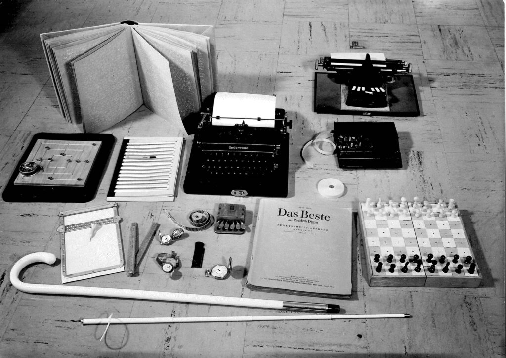 Schwarz/Weiss Aufnahme von alten Gegenständen wie Blindenstock, Gehhilfe, Schachbrett und Bücher