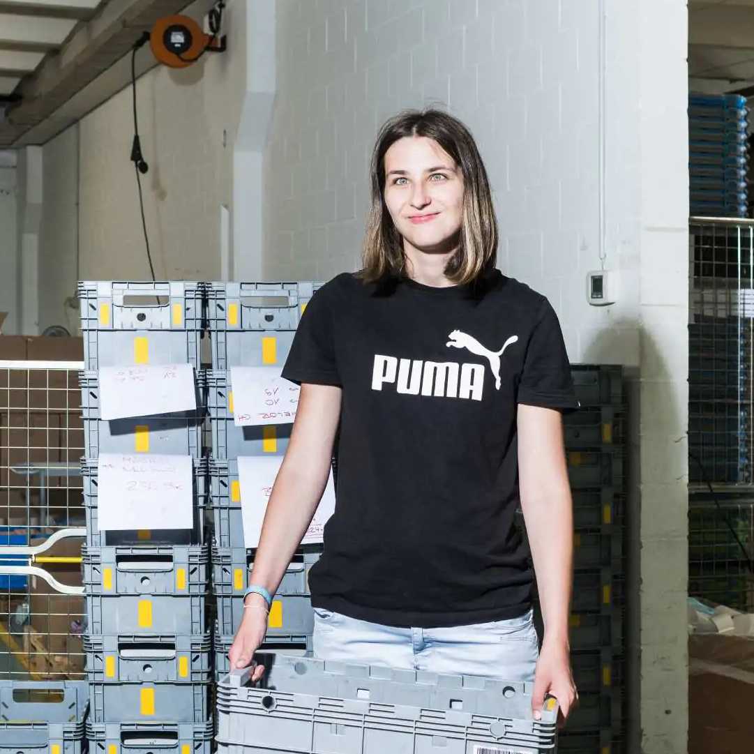 Junge Frau mit einer grauen Kiste in der Hand die in die Kamera lacht.