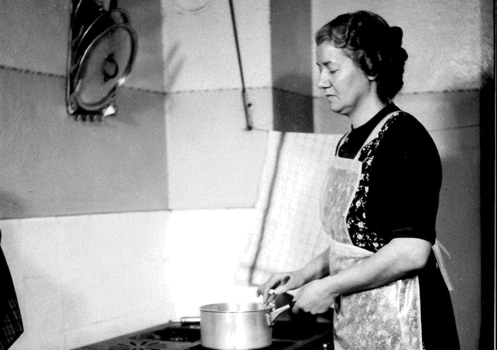 Schwarz/Weiss Aufnahme einer blinden Frau die im Jahr 1930 in der Küche kocht. 