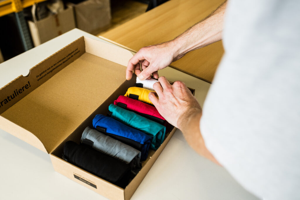 Person die farbige Textilien in eine Schachtel abpackt.