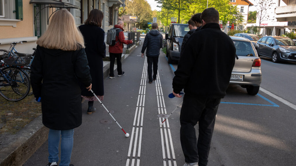 Kleine Gruppe folgt mit einem Langstock den Leitlinien nach.