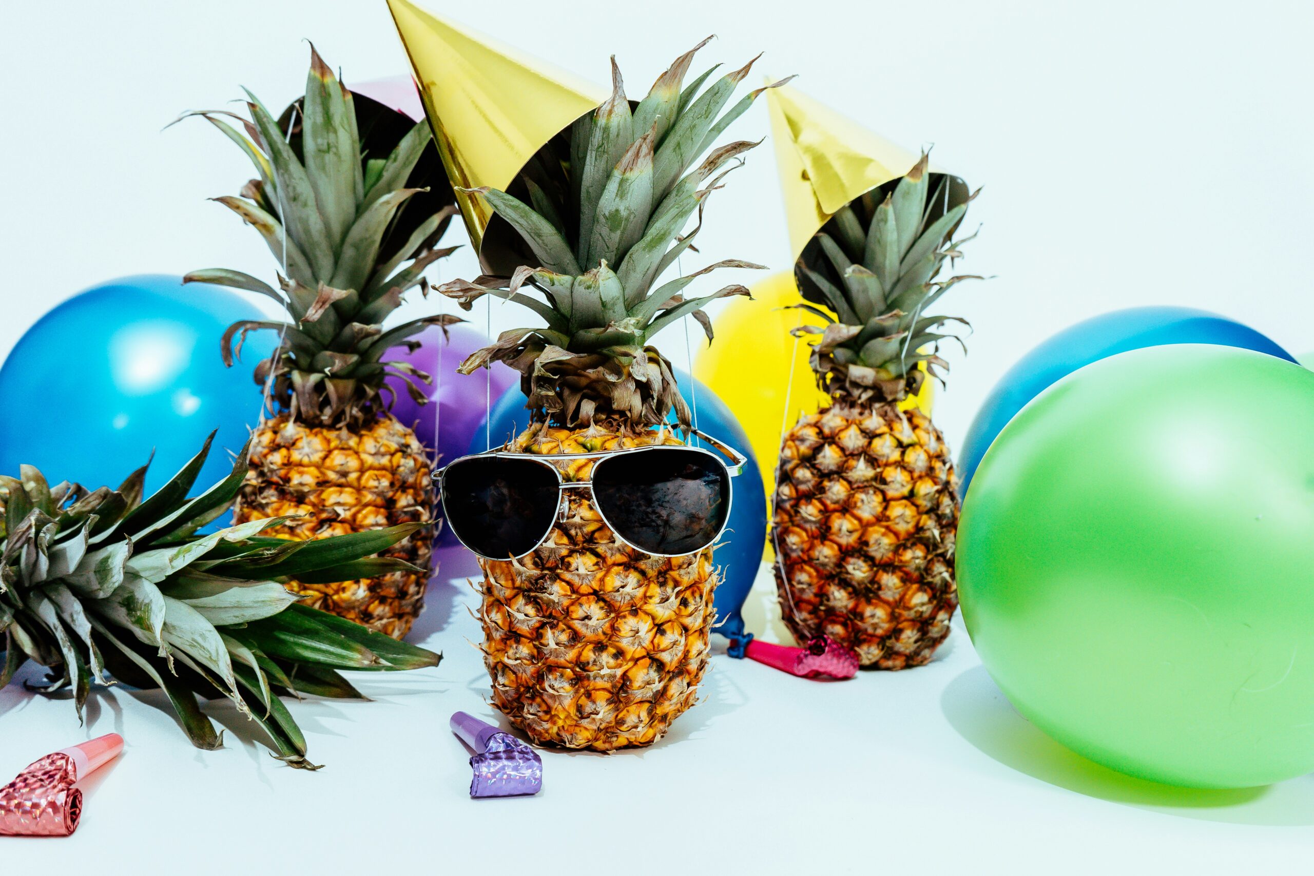 Ananas mit Sonnenbrille und Partyhut, neben bunten Luftballons